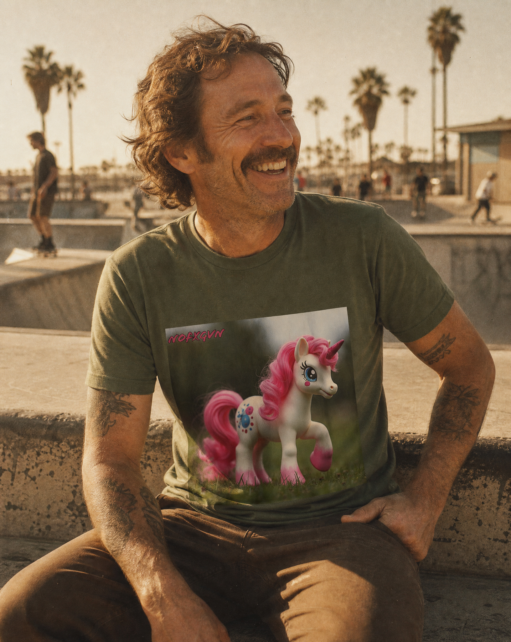 Man sitting at a sunlit skate park in the Vintage Pink Unicorn tee, palm trees behind him